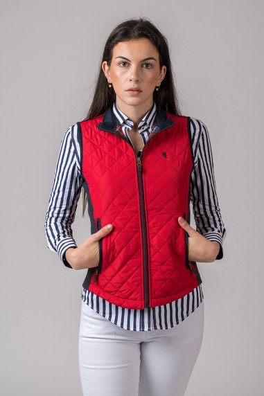 Colete feminino vermelho acolchoado com fecho e bolsos, sobre camisa às riscas e calças brancas