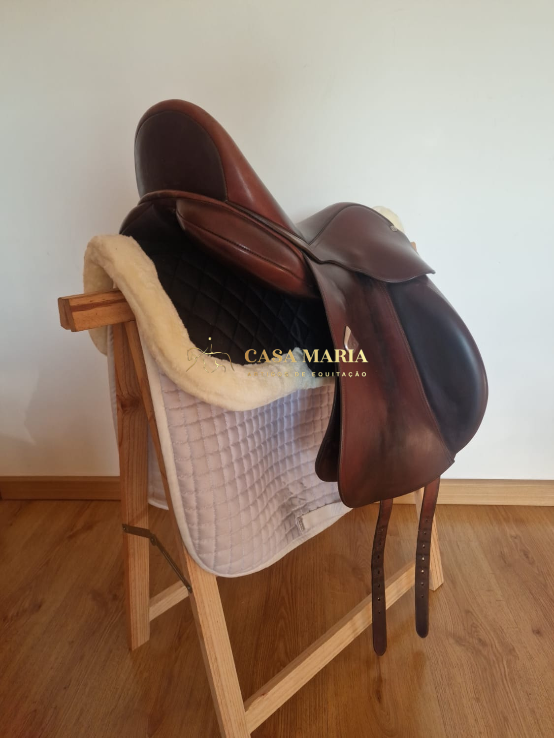 Sela de equitação castanha com manta branca sobre suporte de madeira