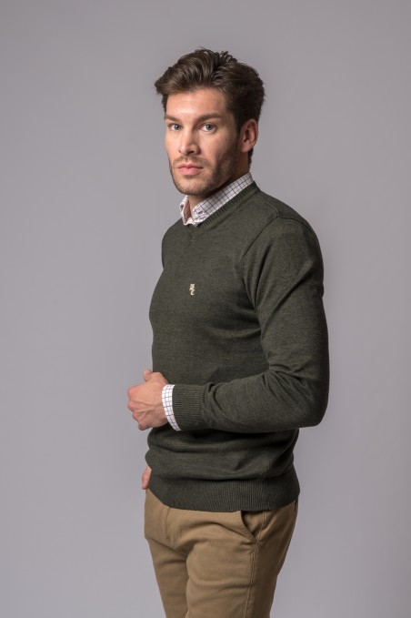 Homem com camisola verde escura, camisa quadriculada e calças bege