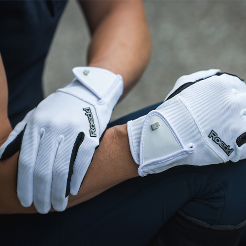Luvas brancas com detalhes pretos e a palavra 'Road' estampada usadas por uma pessoa.