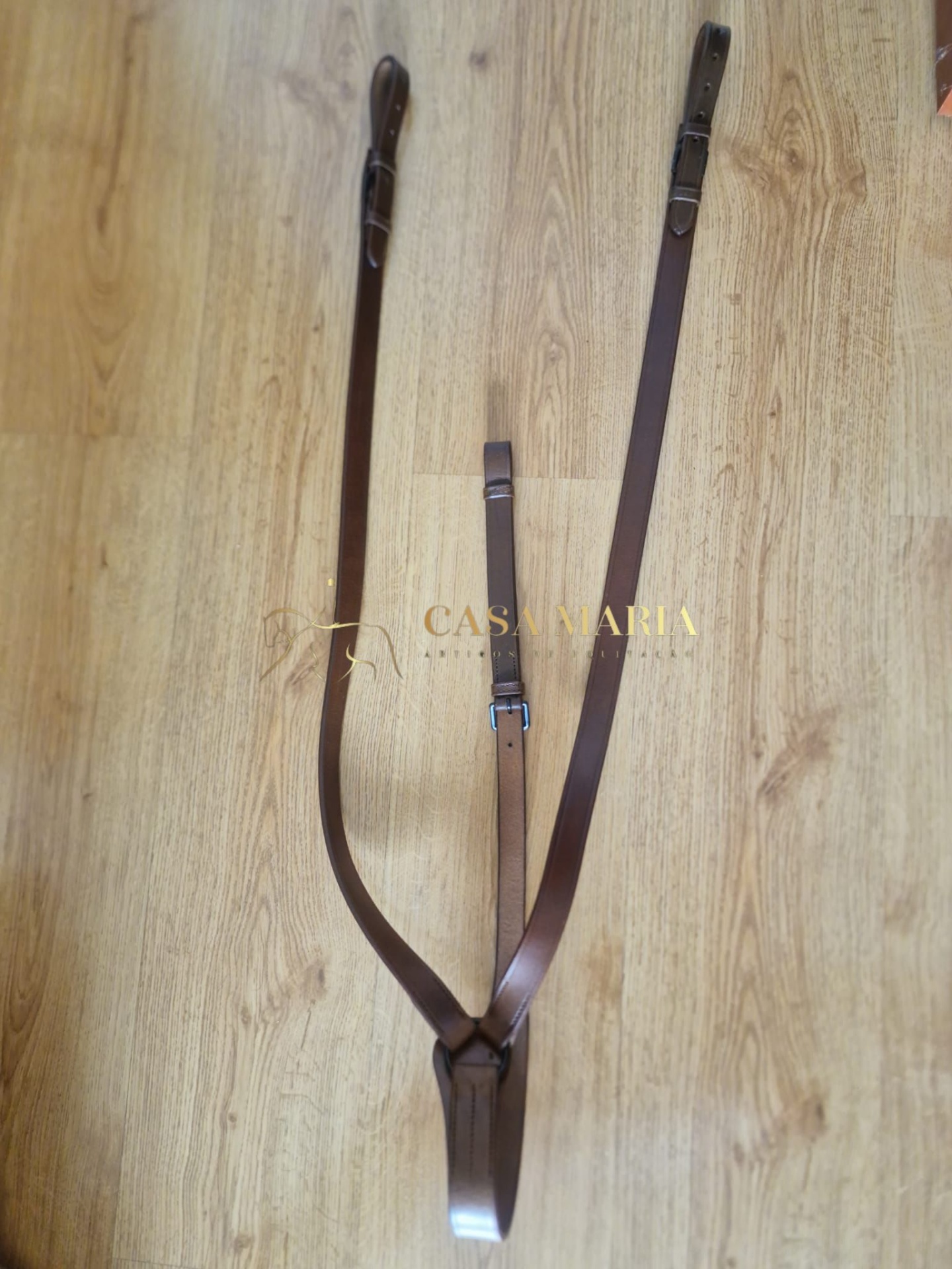 Correia de cabedal castanho escuro com fivelas metálicas prateadas num chão de madeira clara