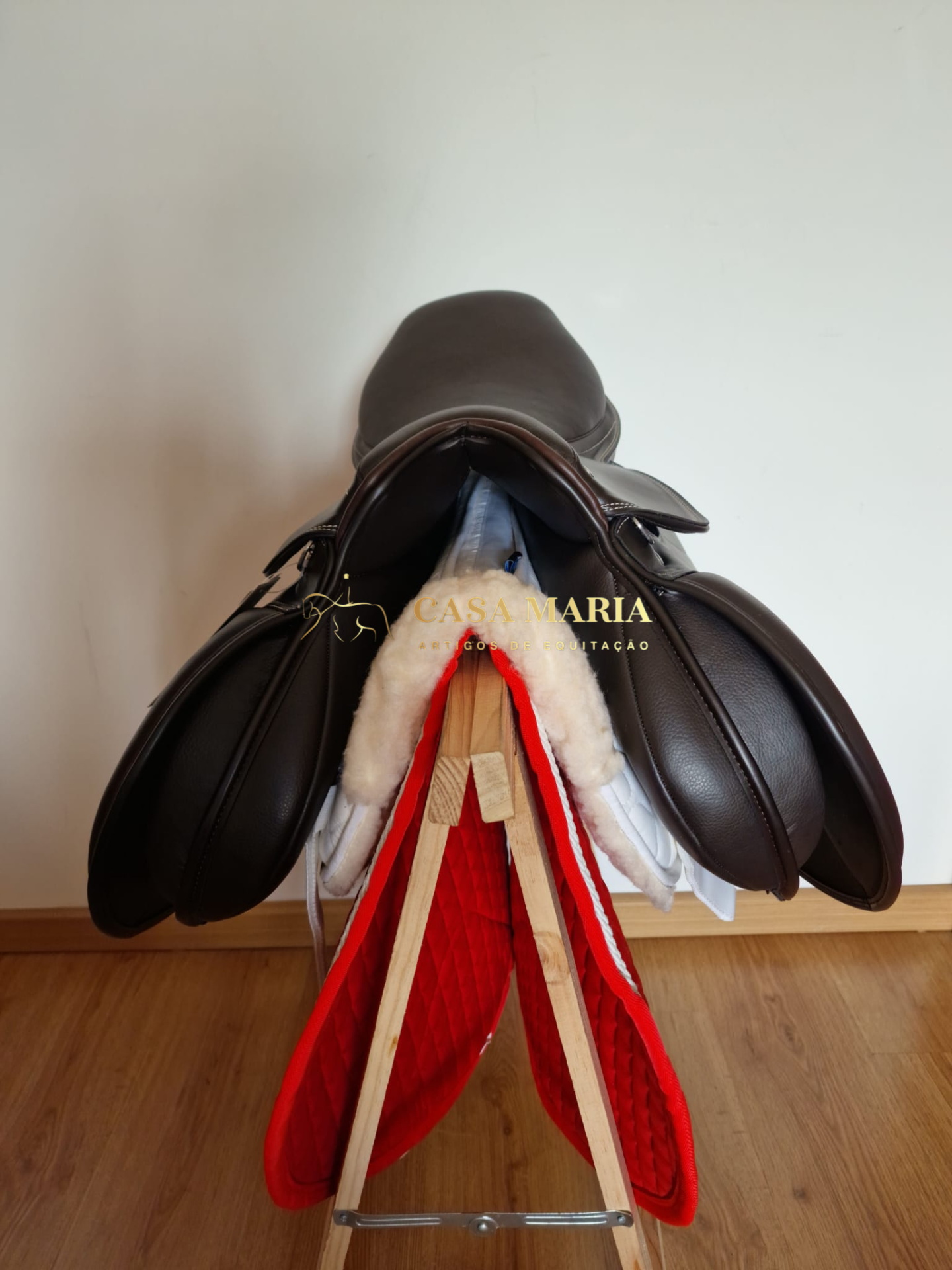 Sela de equitação em couro castanho escuro com mantas vermelhas e brancas em suporte de madeira