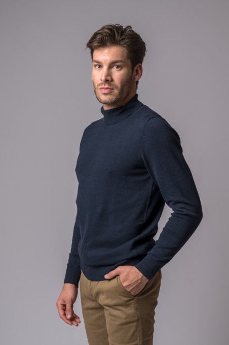 Homem com camisola de gola alta azul escuro e calças castanhas