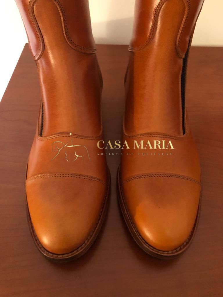 Botas de pele castanha clara em superfície de madeira escura com logo CASA MARIA