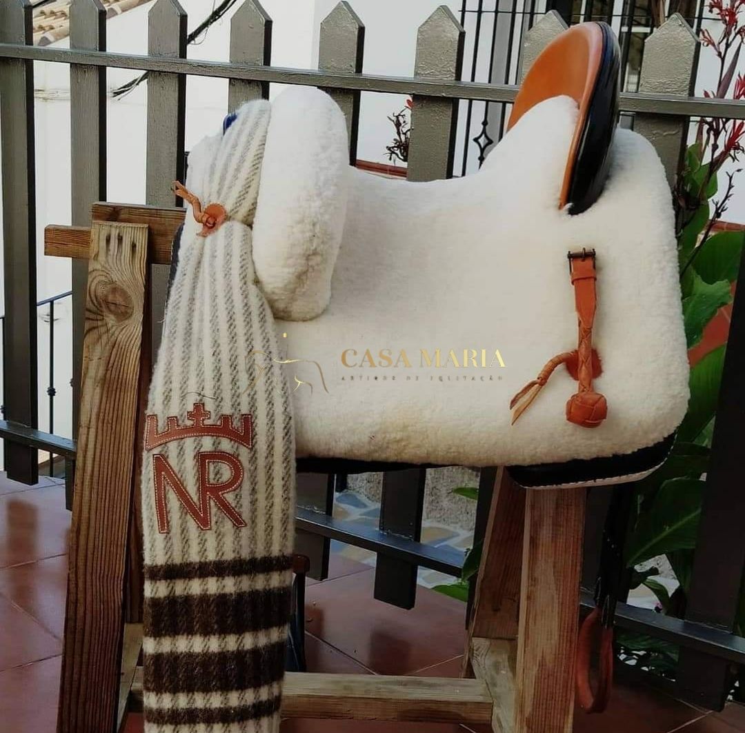 Sela branca macia com detalhes castanhos e cachecol às riscas colgado num suporte de madeira