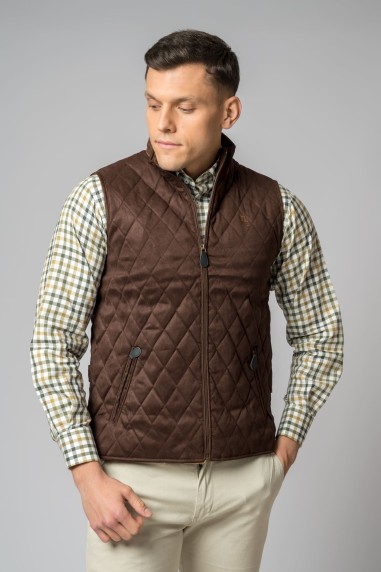 Homem com colete acolchoado castanho e camisa de manga comprida aos quadrados.