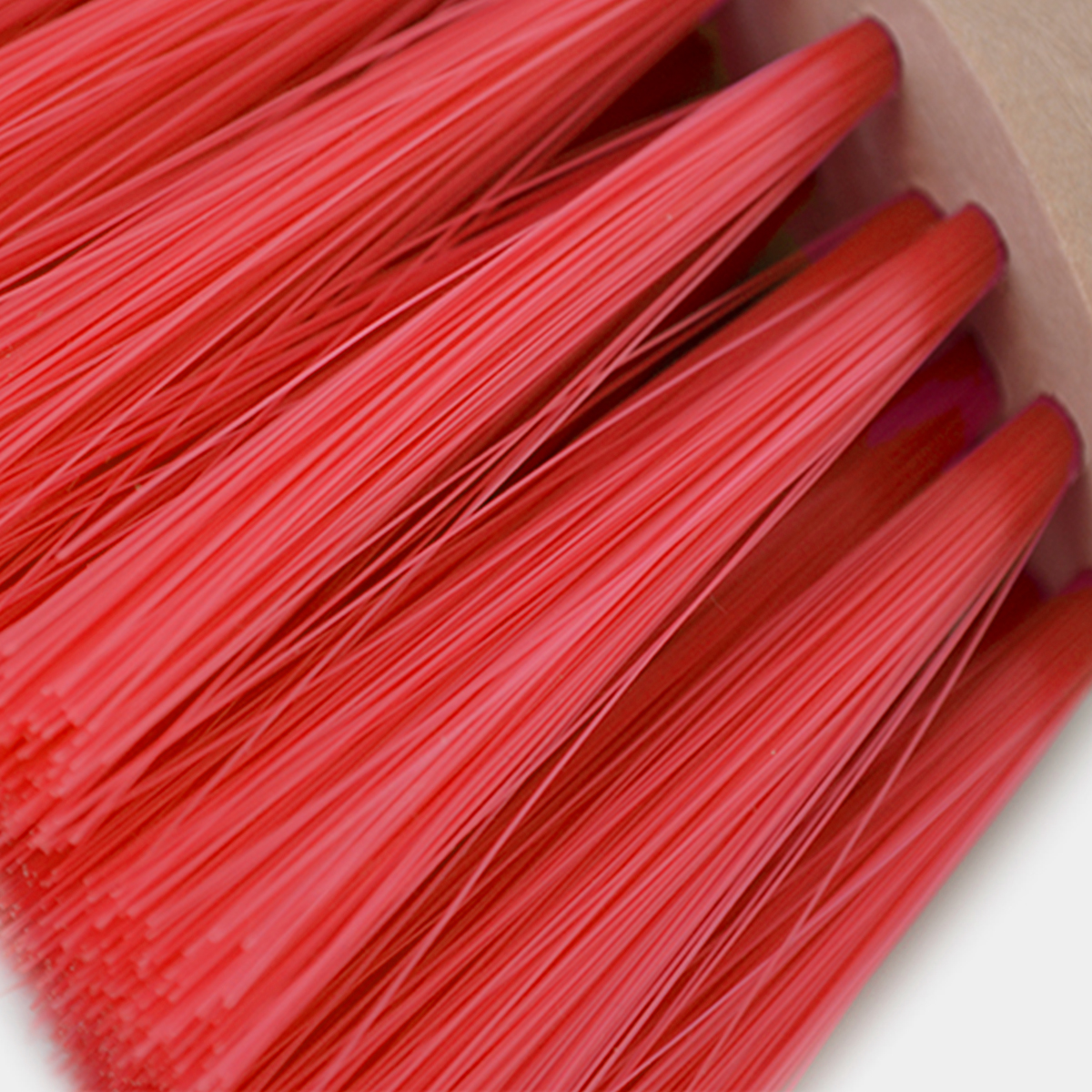 Vassoura com cerdas vermelhas e base de madeira clara em fundo branco