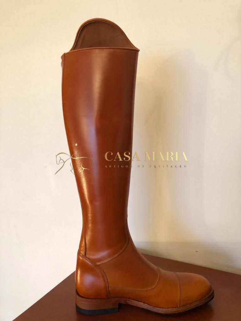 Bota alta castanha de couro em exibição sobre móvel de madeira contra parede clara