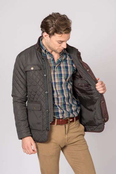Homem a usar casaco acolchoado preto aberto mostrando o forro castanho e camisa xadrez azul e verde, com calças castanho claro