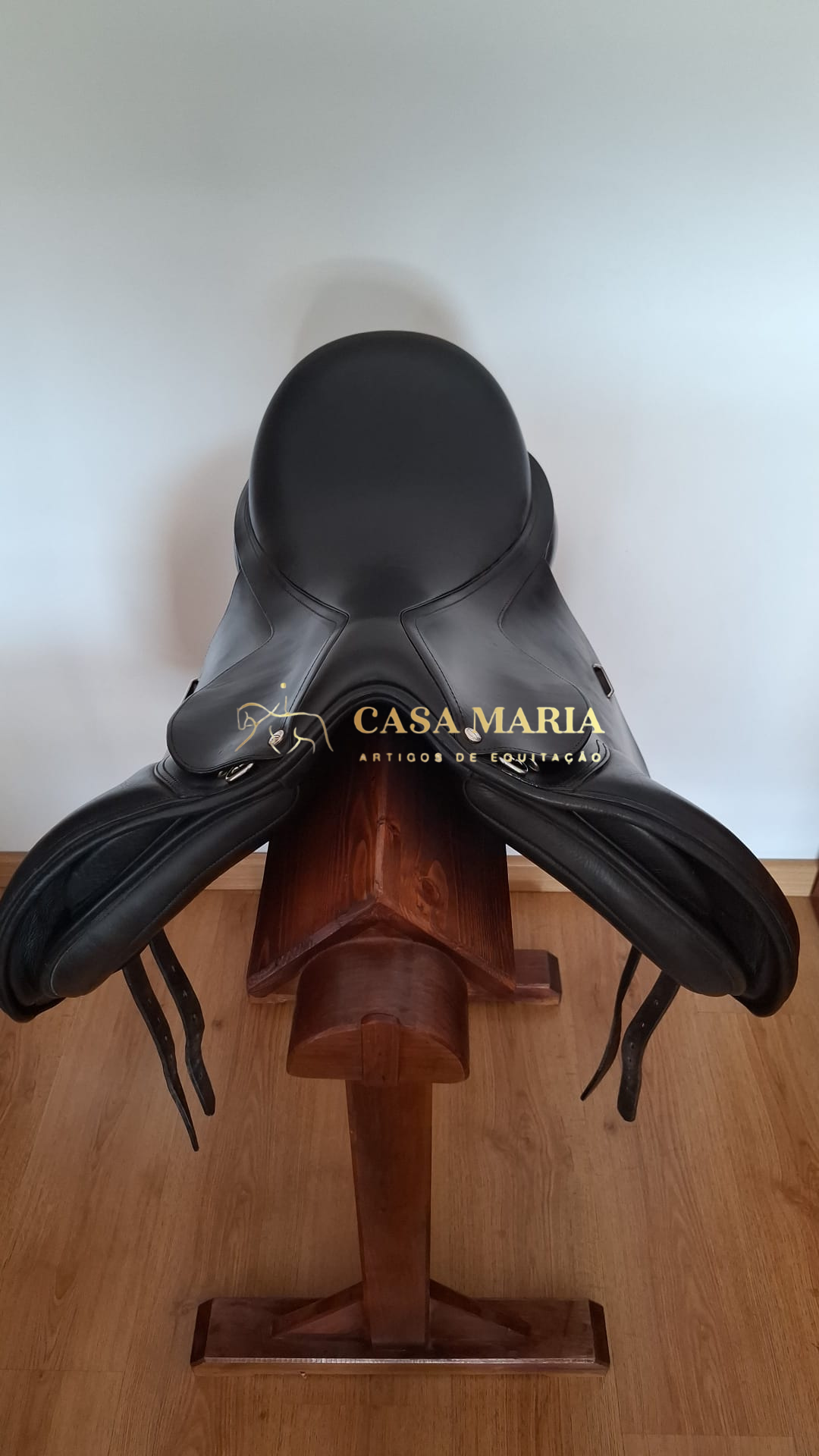 Sela de equitação preta em suporte de madeira com logo CASA MARIA