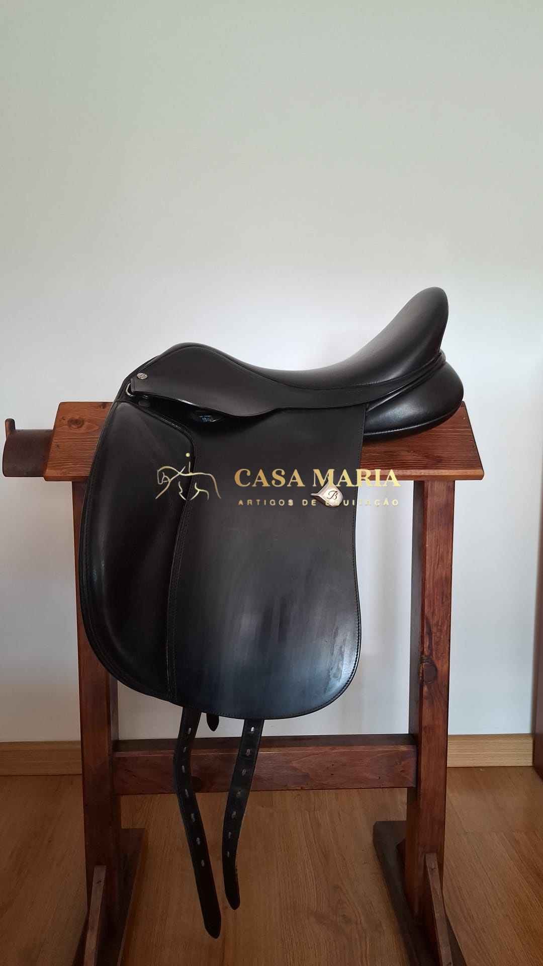 Sela de equitação de pele preta pendurada num suporte de madeira