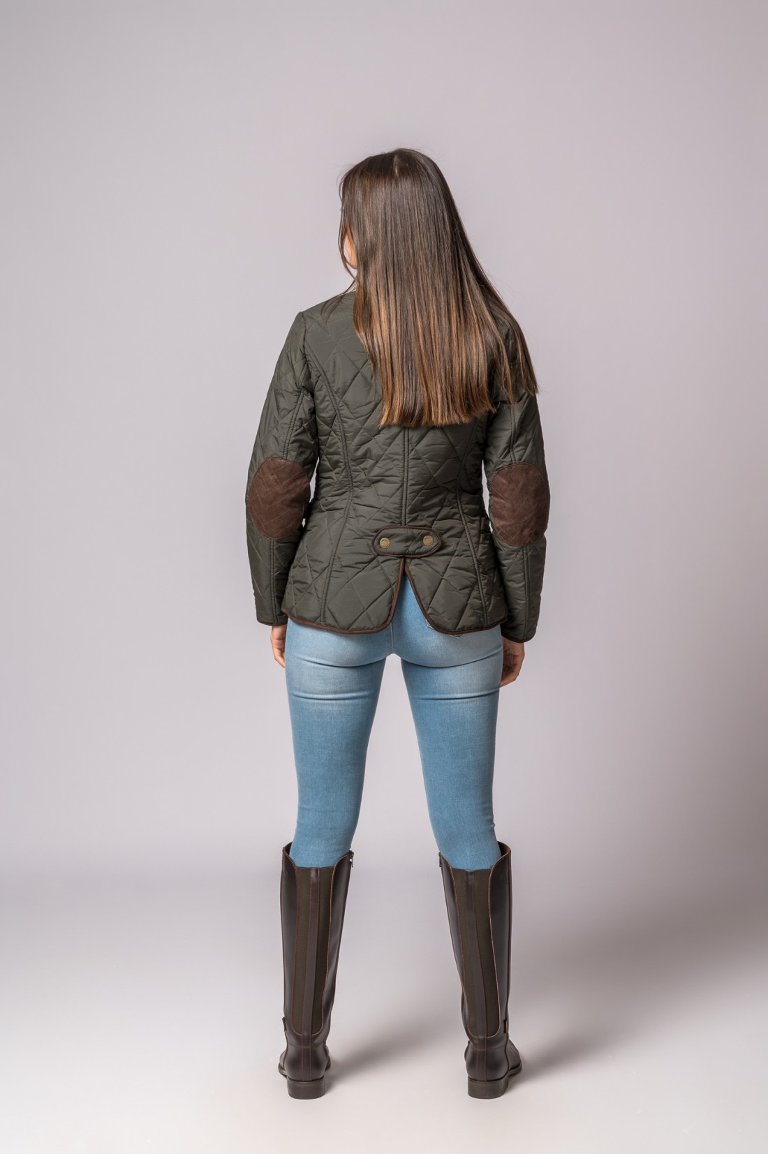Vista de costas de pessoa com casaco verde acolchoado, calças de ganga e botas castanhas