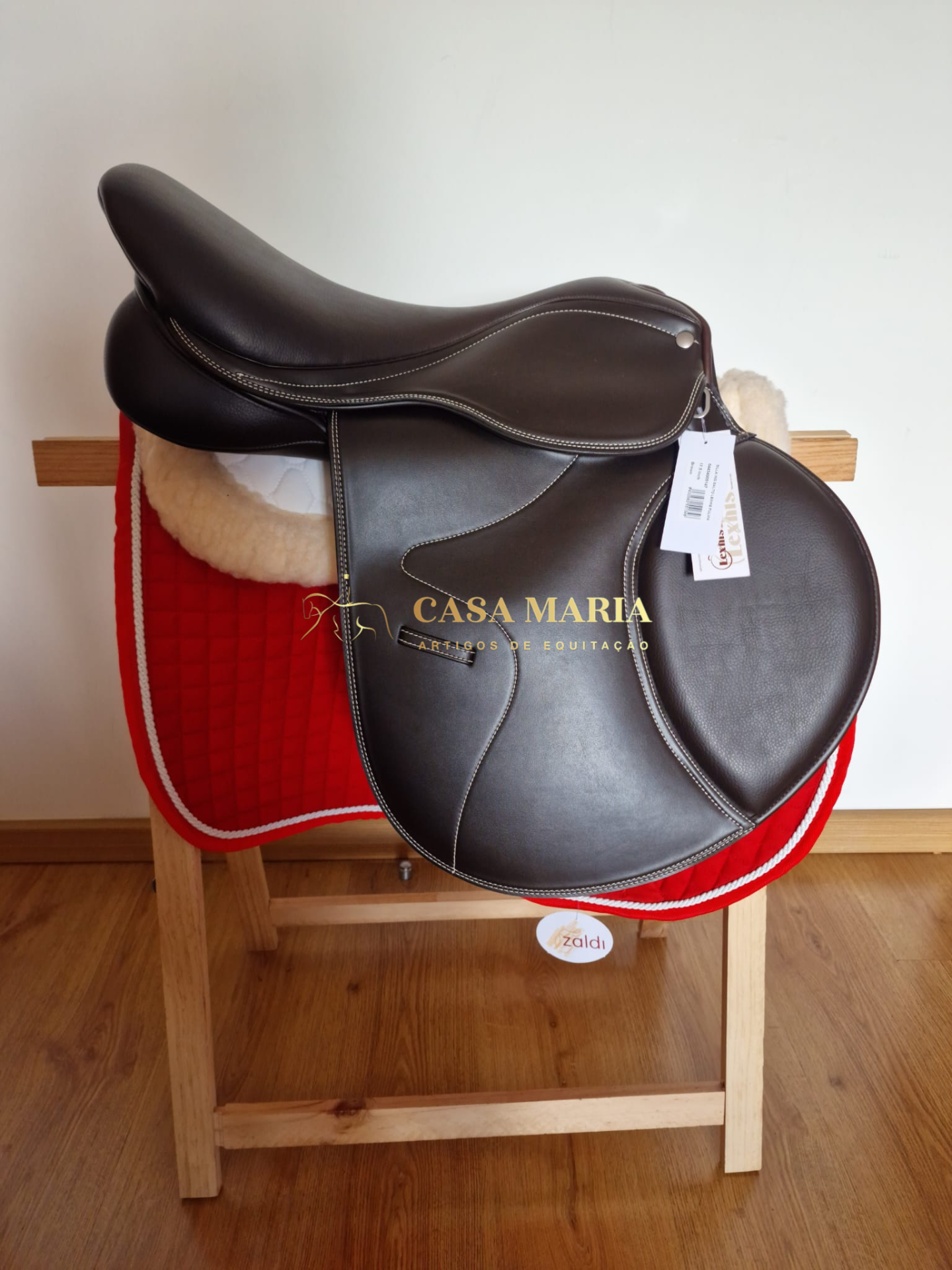 Sela de equitação preta em couro numa manta vermelha sobre estrutura de madeira