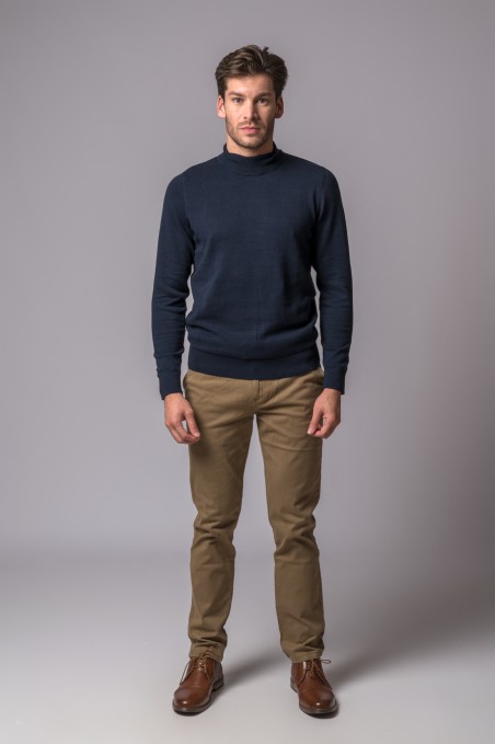 Homem com camisola de malha azul escura, calças bege e sapatos castanhos