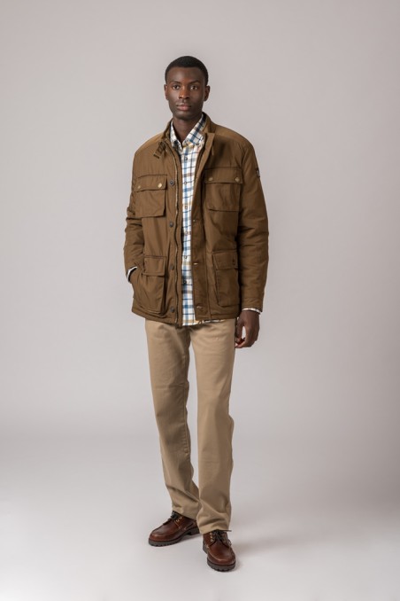 Homem com casaco castanho, camisa xadrez, calças bege e sapatos castanhos.