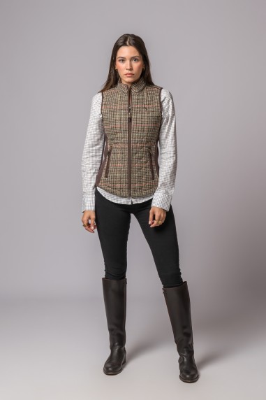 Mulher vestindo colete pied-de-poule castanho, camisa branca xadrez azul, calças pretas e botas castanhas