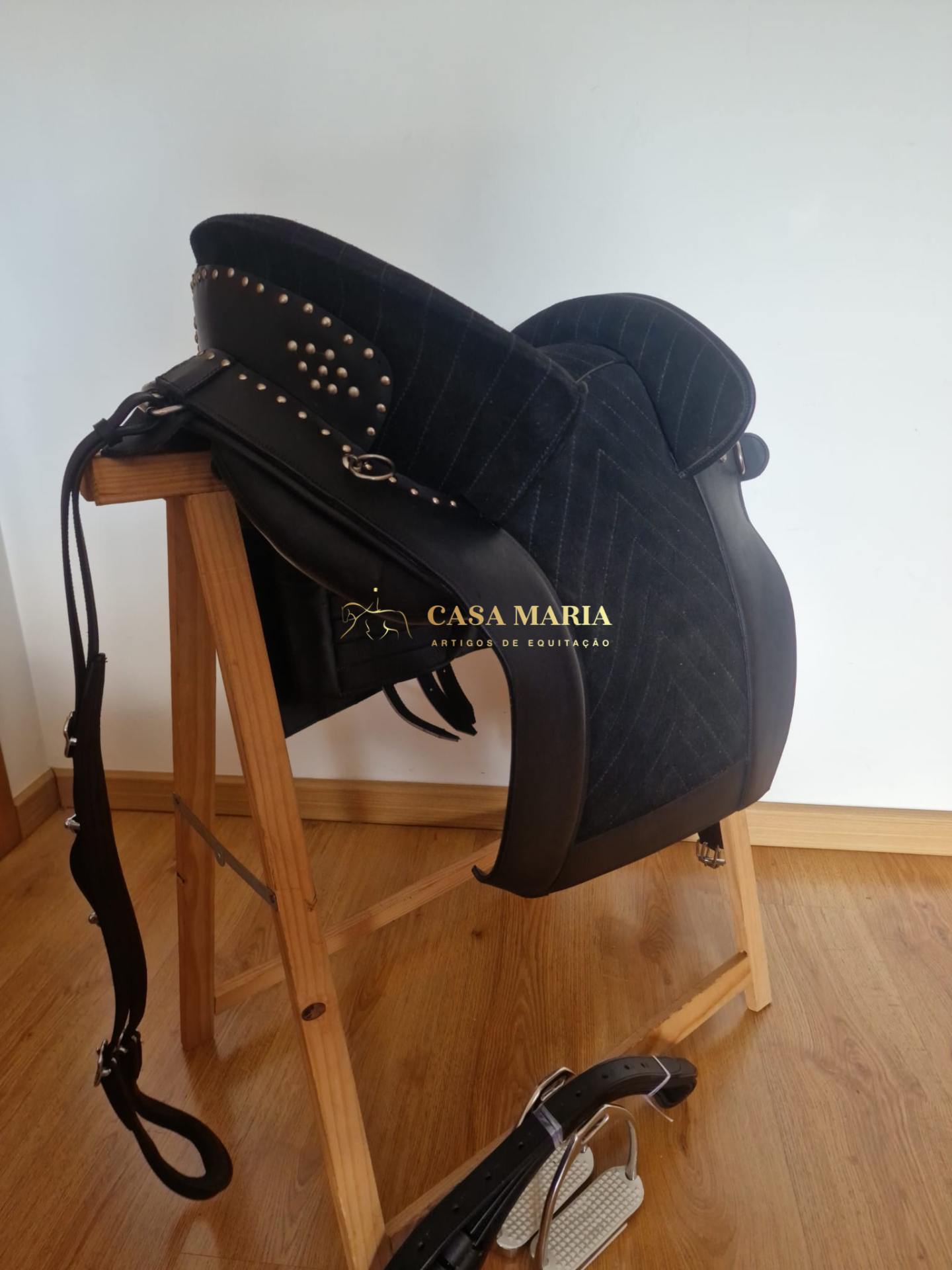 Sela de equitação preta com tachas metálicas sobre suporte de madeira