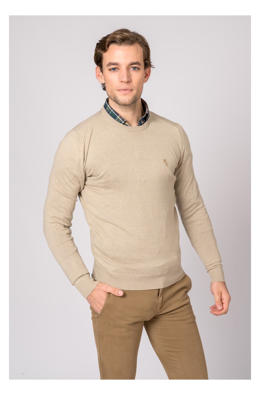 Homem com camisola bege e camisa xadrez a posar contra fundo branco