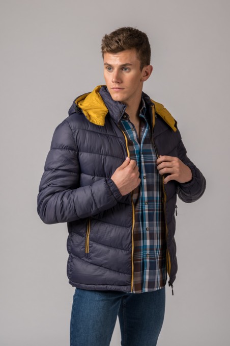 Homem a usar casaco acolchoado azul escuro com interior amarelo e capuz, camisa xadrez e calças de ganga