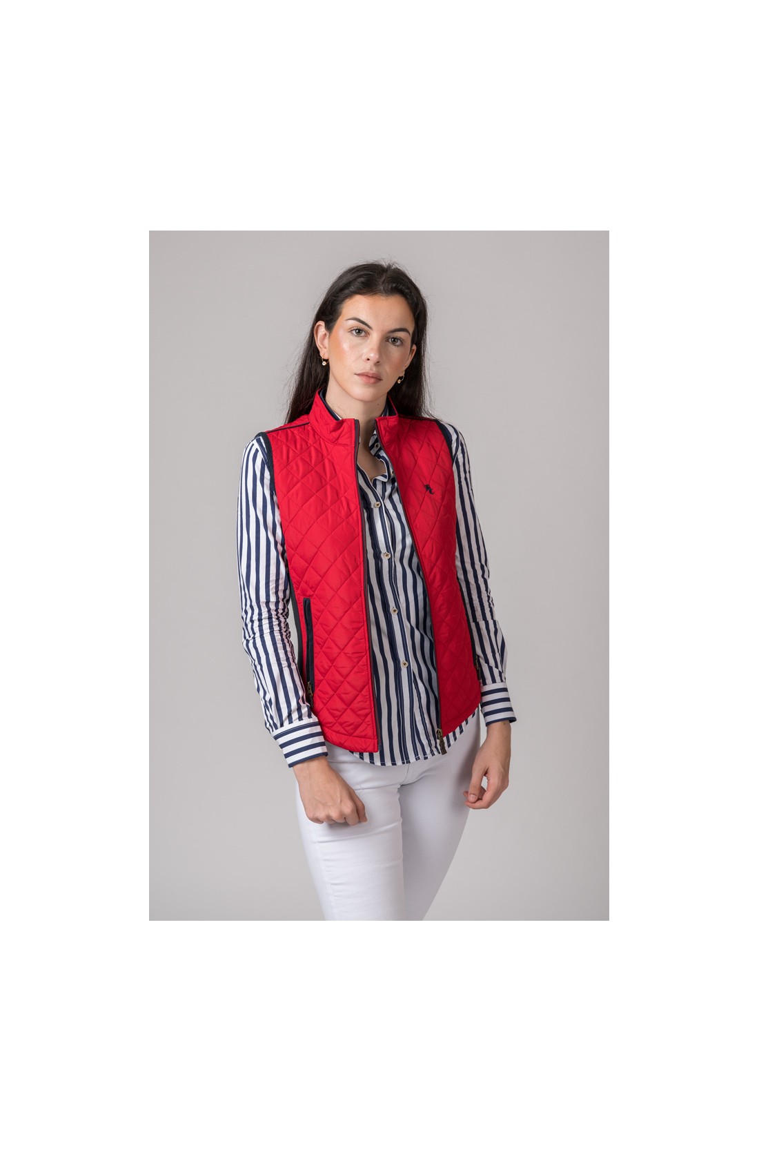 Mulher com colete vermelho e camisa às riscas em fundo cinzento