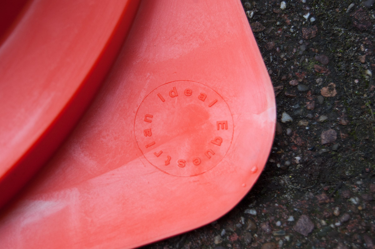 Cones de sinalização laranja em plástico empilhados sobre asfalto com inscrição circular Ideal Equipamentos.