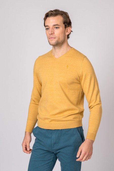 Homem com camisola amarela de malha e calças azuis em fundo branco