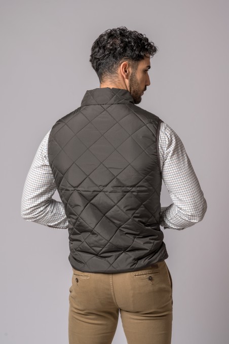 Homem de costas com colete acolchoado cinza escuro, camisa xadrez e calças castanhas