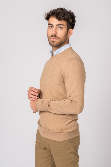 Homem com camisola bege e camisa azul clara, calças castanhas, fundo cinzento claro