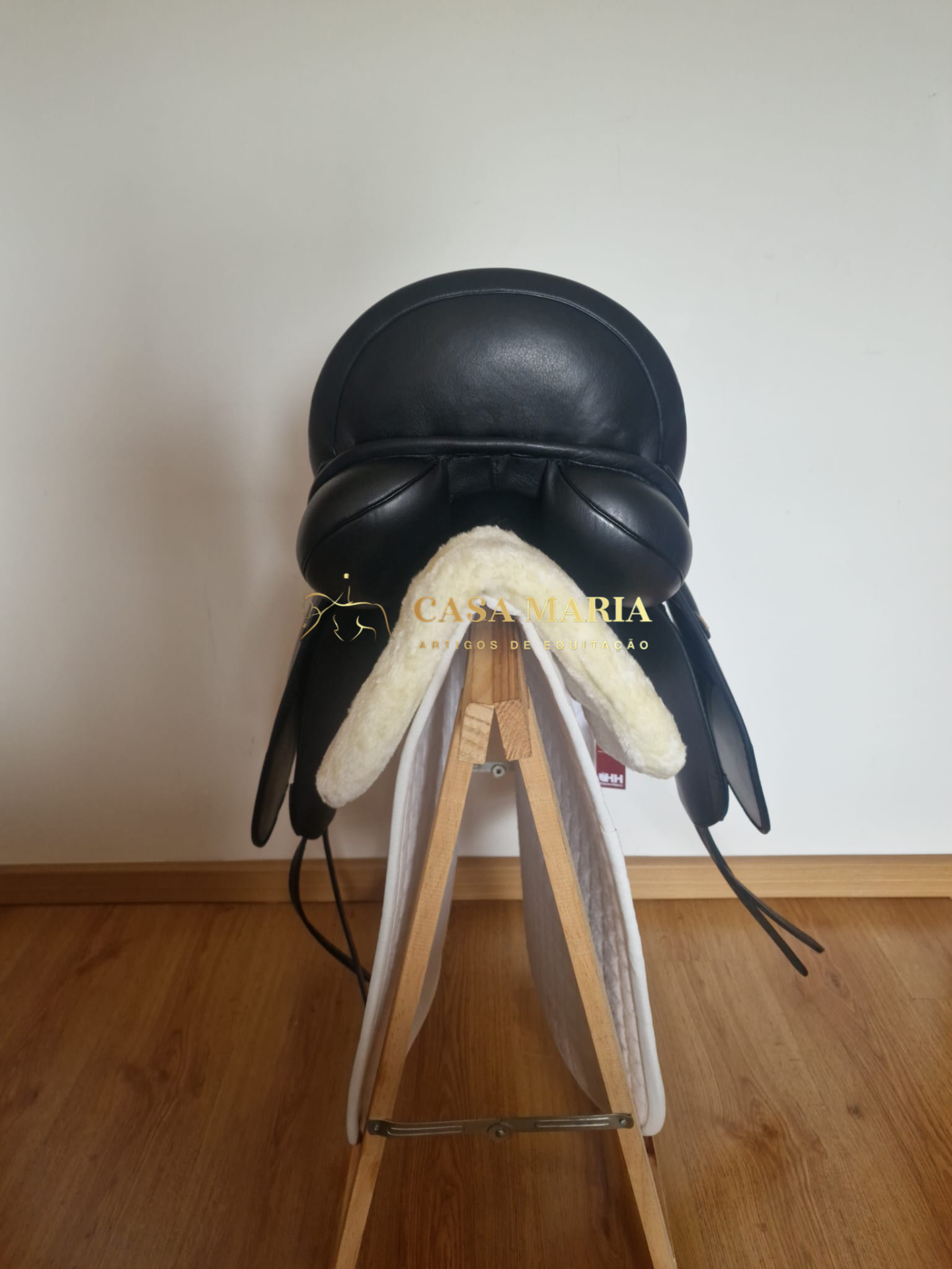 Sela equestre preta em suporte de madeira com almofada e manta brancas