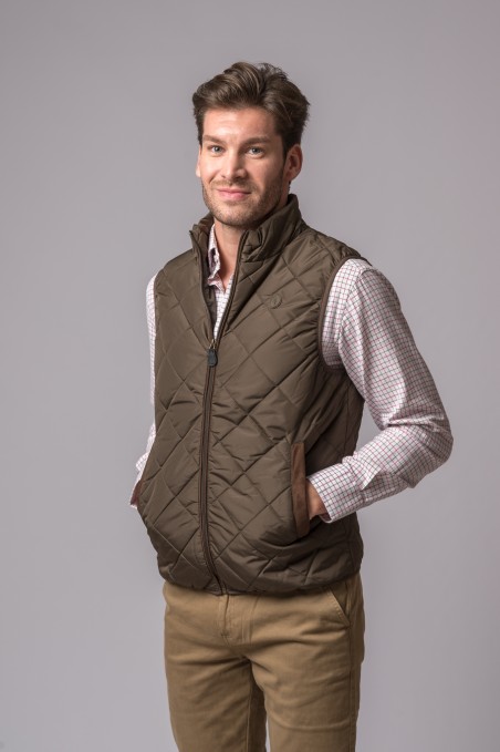 Homem com colete acolchoado verde-oliva sobre camisa quadriculada e calças cáqui