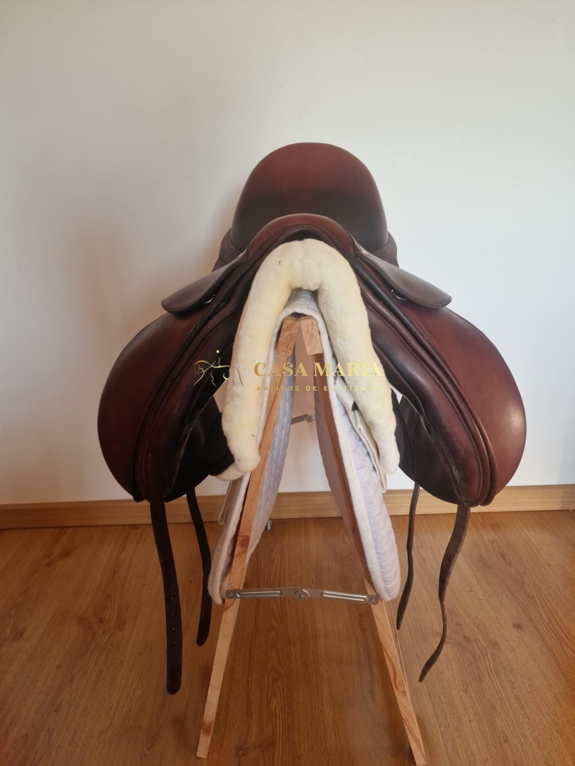 Sela de equitação castanha em suporte de madeira com forro de lã branca