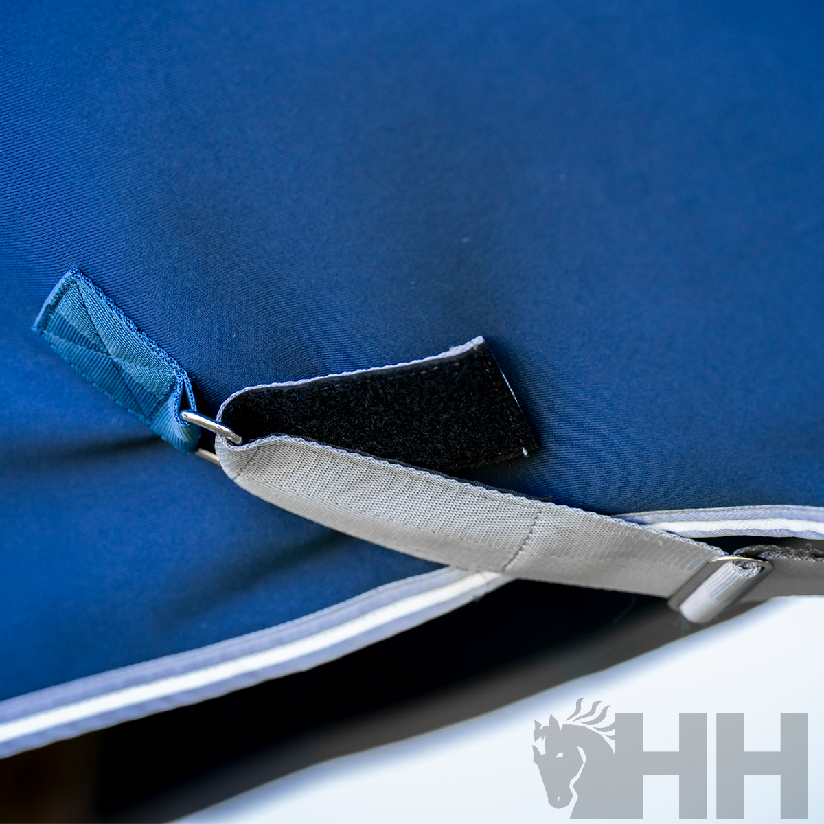 Detalhe de tecido azul com fita cinza e velcro preto num canto reforçado.