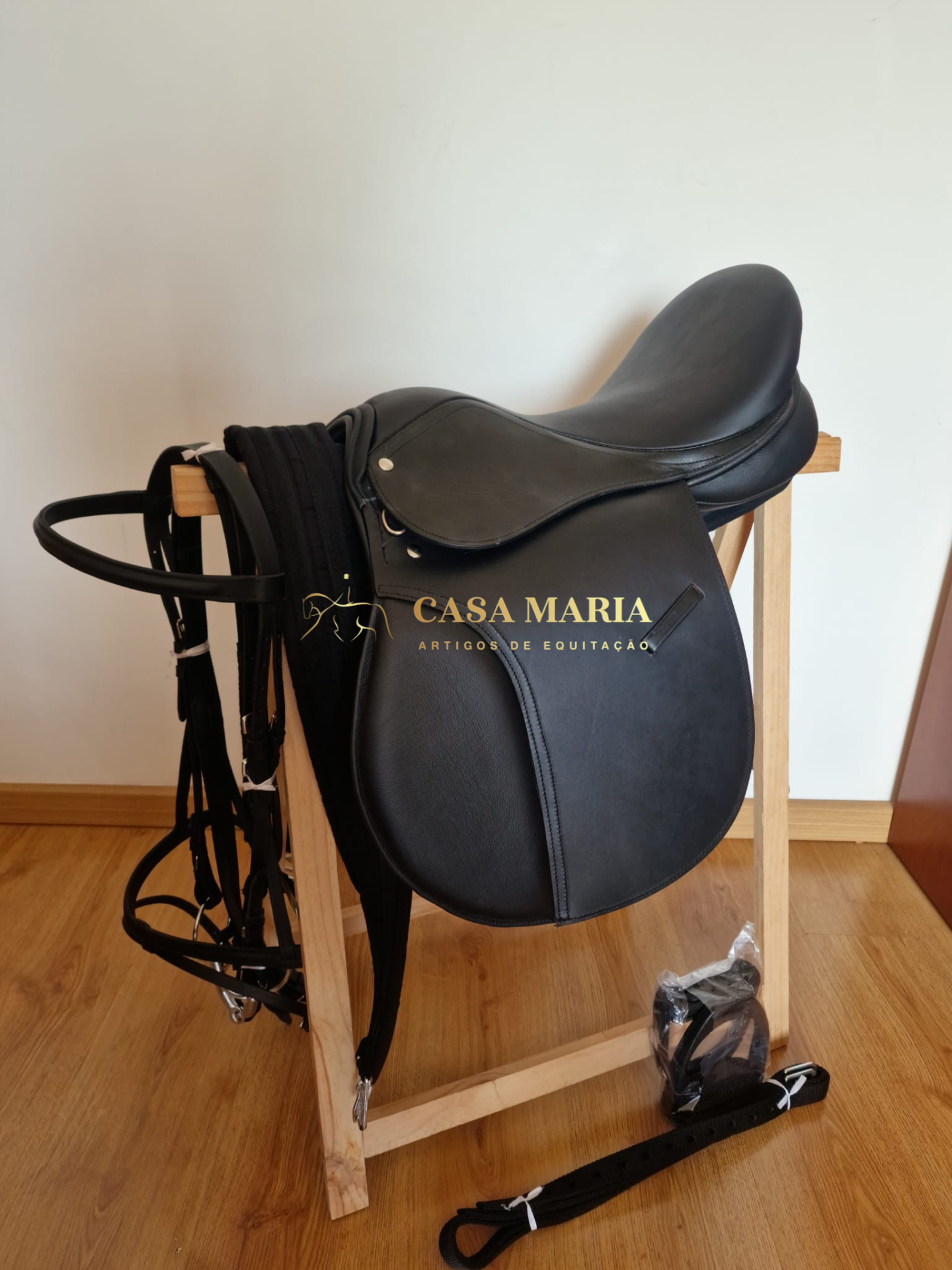 Sela de equitação em couro preto num suporte de madeira com acessórios em preto