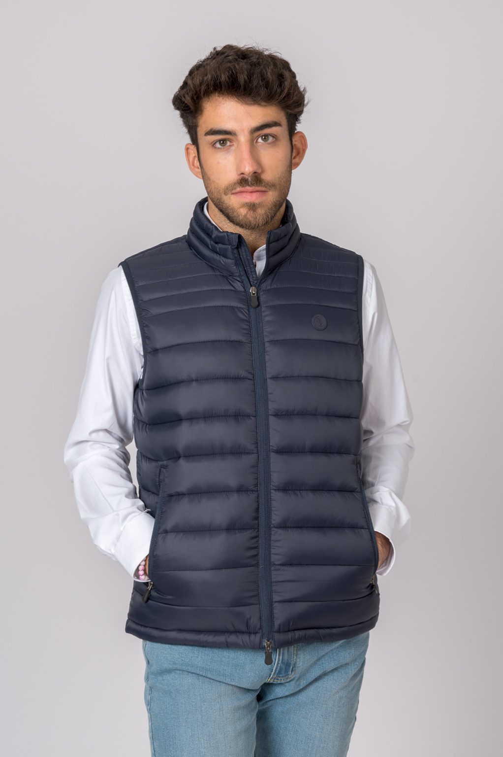 Homem com colete acolchoado preto e camisa branca em fundo cinza