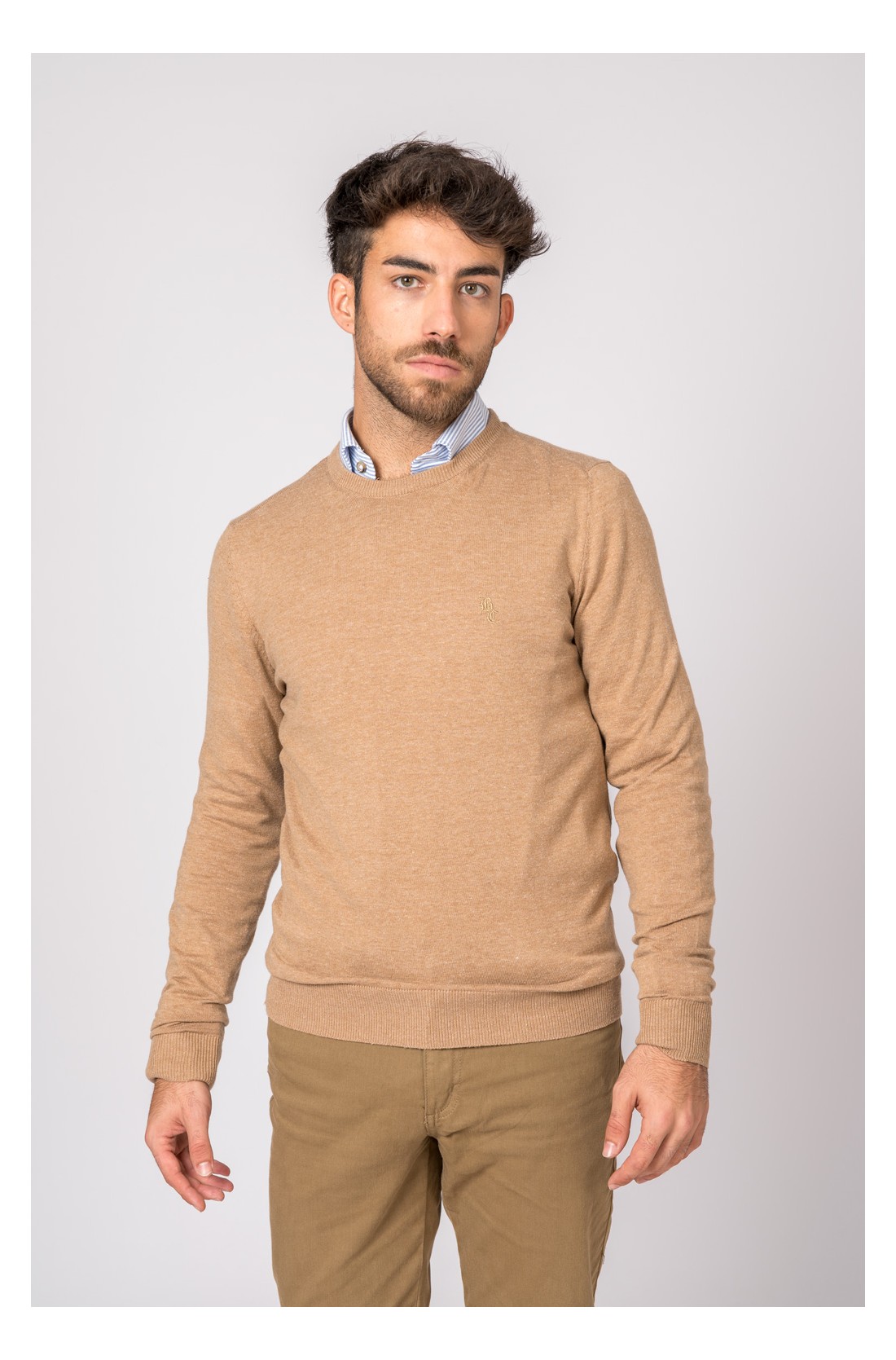 Homem com camisola castanha e camisa azul clara em fundo branco