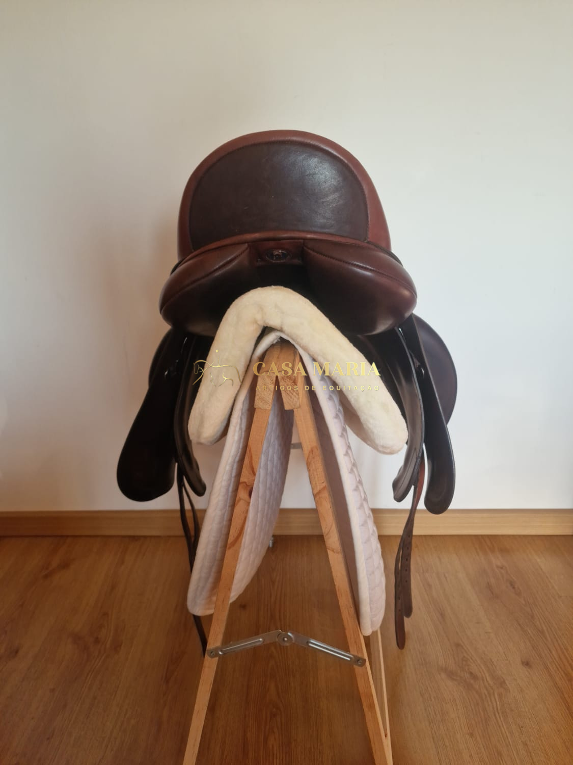 Sela de equitação de couro castanho escuro com manta branca num suporte de madeira