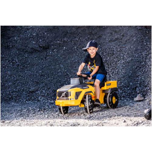 Criança num trator amarelo de brinquedo em terreno de cascalho