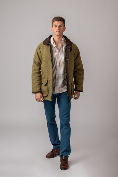 Homem com casaco verde-oliva, camisa aos quadrados, calças azuis e sapatos castanhos
