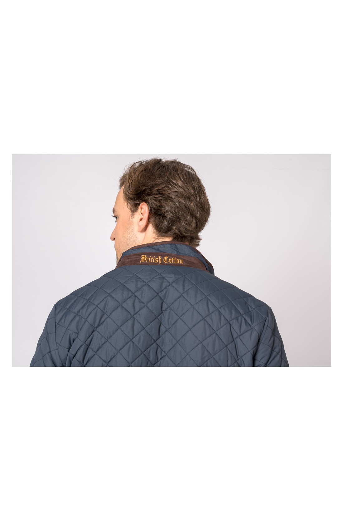 Casaco acolchoado azul escuro com gola castanha e texto 'British Cotton'.