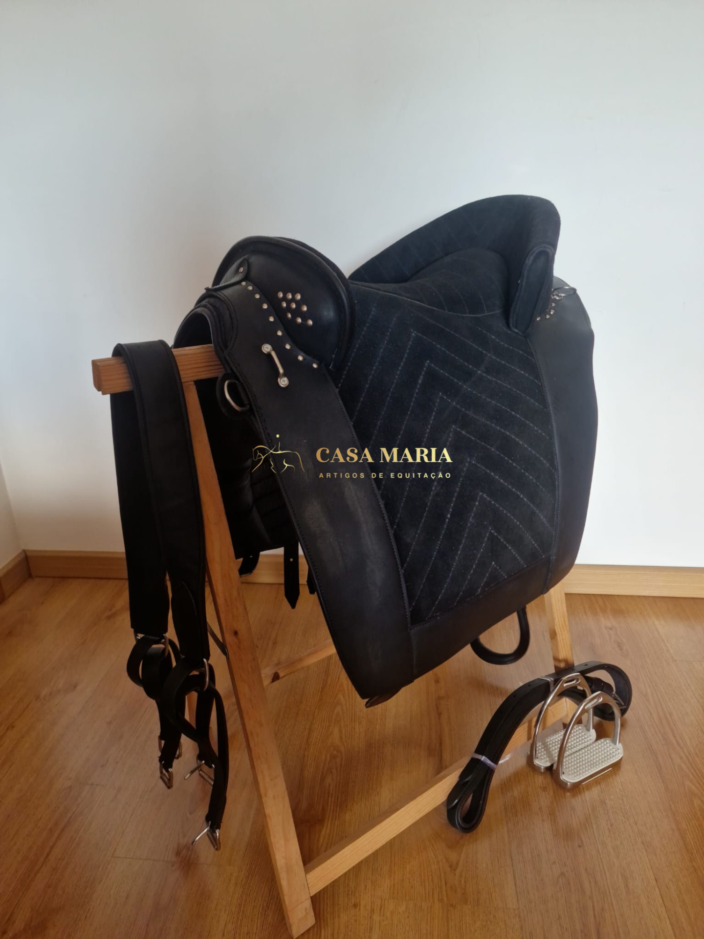 Sela preta de equitação com detalhes metálicos sobre suporte de madeira