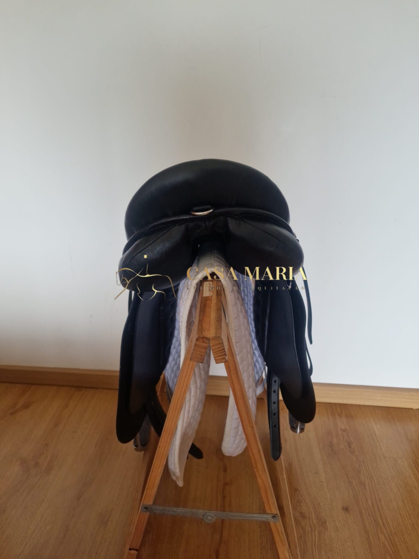 Sela de equitação preta em couro num suporte de madeira com protetor branco.