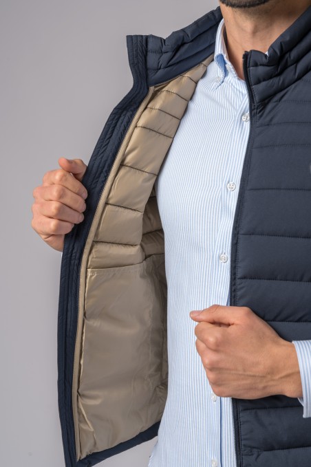 Colete acolchoado azul escuro com forro bege aberto em pessoa com camisa azul clara