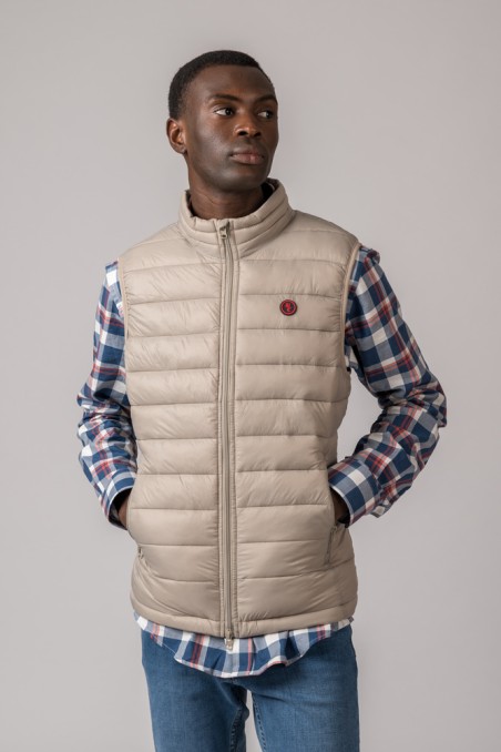 Homem a usar colete acolchoado bege com camisa xadrez e calças de ganga