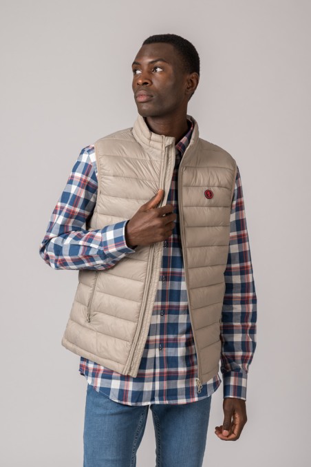 Homem a usar colete bege acolchoado e camisa xadrez azul