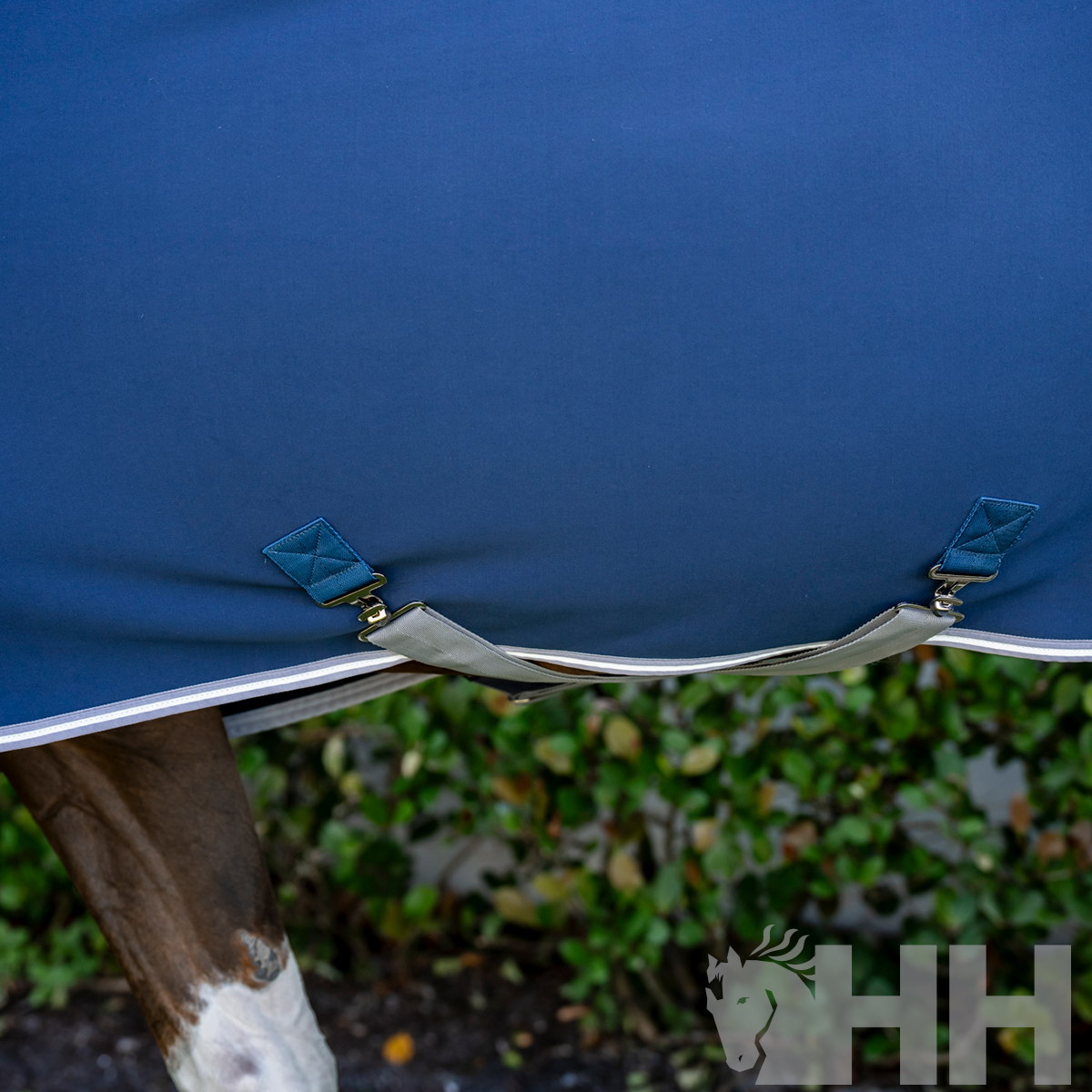 Manta azul para cavalo com fechos metálicos e detalhes em branco e azul sobre perna do cavalo