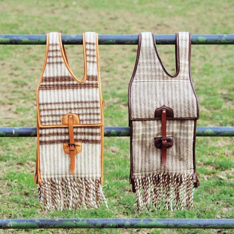 Dois sacos mochila de tecido xadrez bege e castanho com franjas, suspensos numa cerca metálica ao ar livre