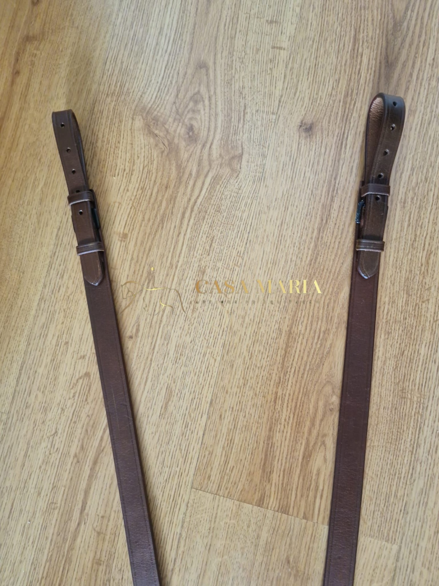 Alças de pele castanha com fivelas metálicas num chão de madeira clara