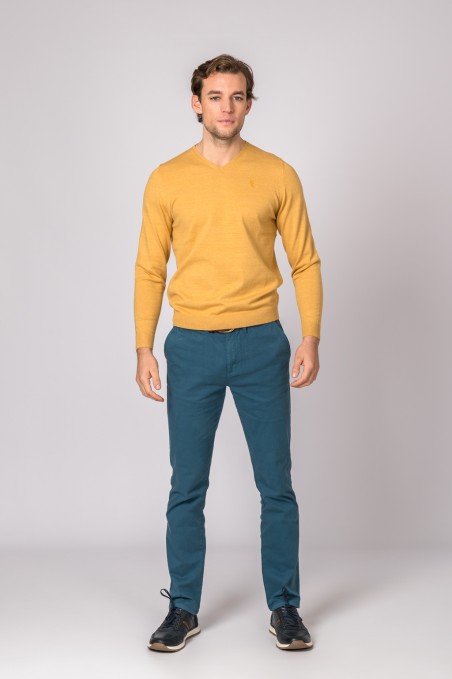 Homem com sweater amarelo, calças azul-escuras e sapatos pretos num fundo cinzento Claro