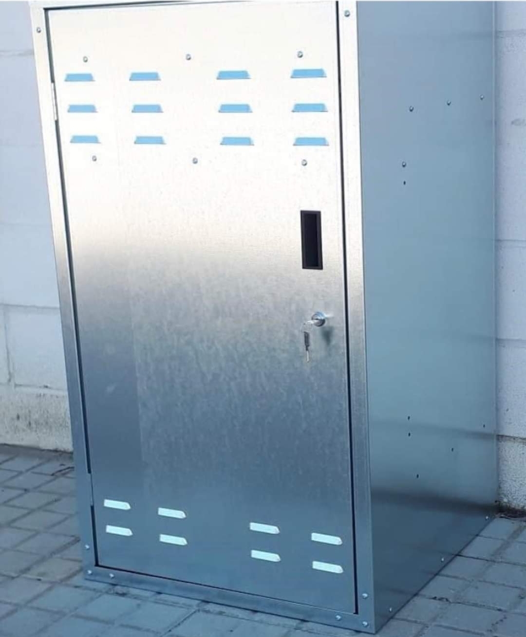 Armário metálico cinza prateado com fechadura e aberturas colocado em pavimento exterior