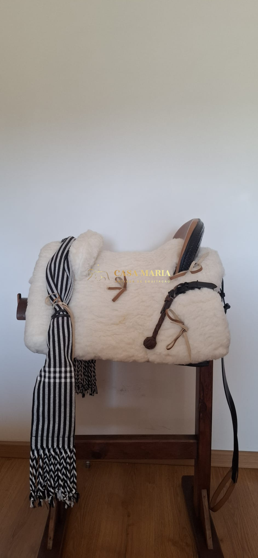 Sela de equitação branca com faixa preto e branca num suporte de madeira